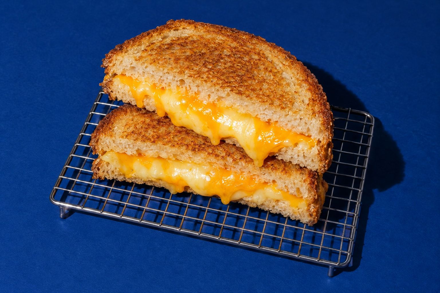 Två halvor av en grillad osttoast staplade på ett galler, med smält cheddar och gouda som rinner ur snittytan.